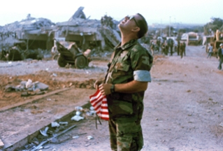 An unidentified Marine holds a flag and stares skyward at the U.S. Marine base after a massive bomb blast that destroyed the base and caused a huge death toll rising to 239, near Beirut airport, Oct. 23, 1983. The number of dead included 218 Marines, 18 Navy men and 3 Army personnel. (AP Photo/Mark Foley)